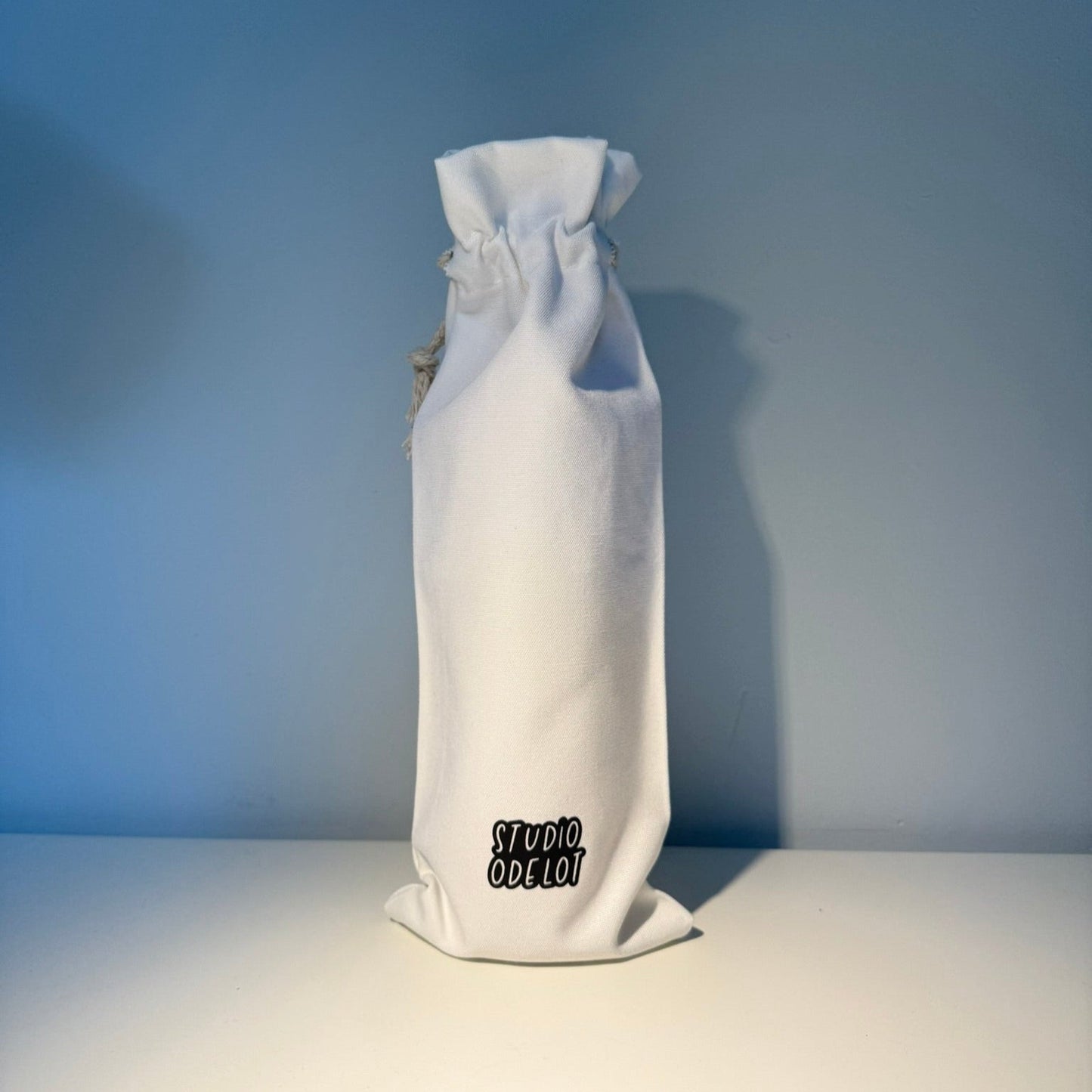 Canvas tas voor wijnfles met de tekst pairs well with a new home - housewarming cadeau - logo achteraan - Studio Odelot